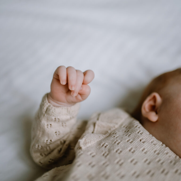 Newborn fotoshoot baby op bed met detail van het hand