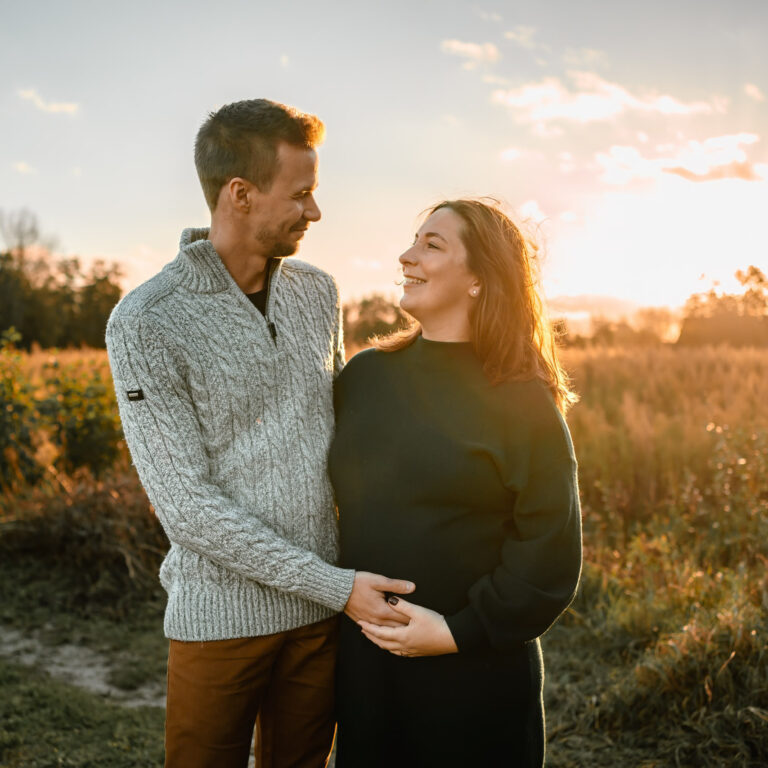 Zwanger koppel bij golden hour met liefdevolle blikken naar elkaar